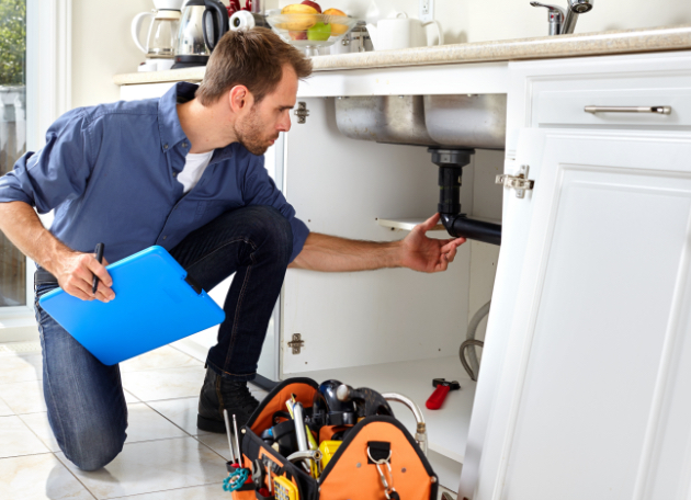 male plumber checking kitchen sink plumbing with a clipboar in hand